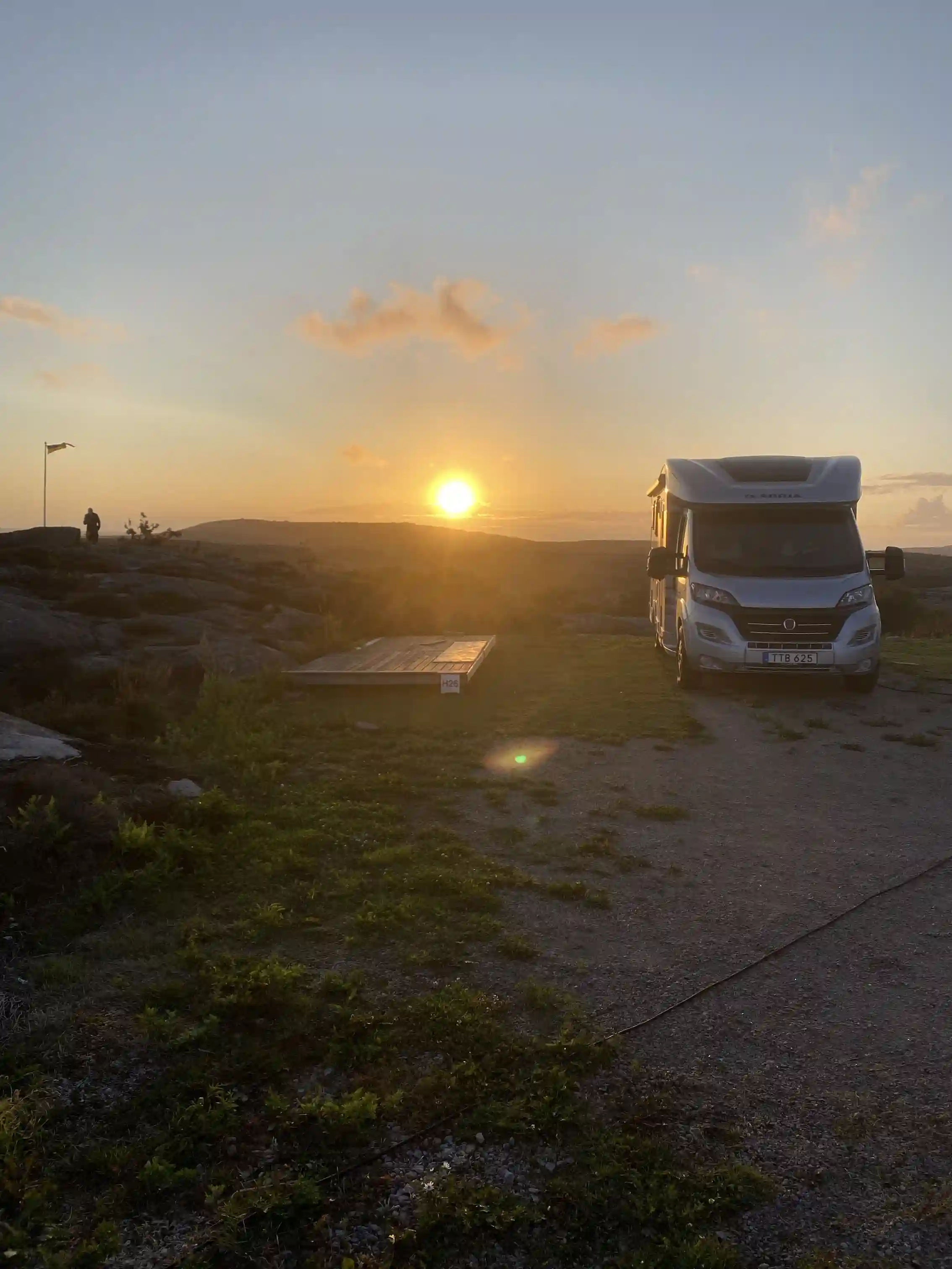 En husbil står parkerad på Sotenäs Camping i solnedgången med en vacker himmel i varma färger och lätta moln vid horisonten.