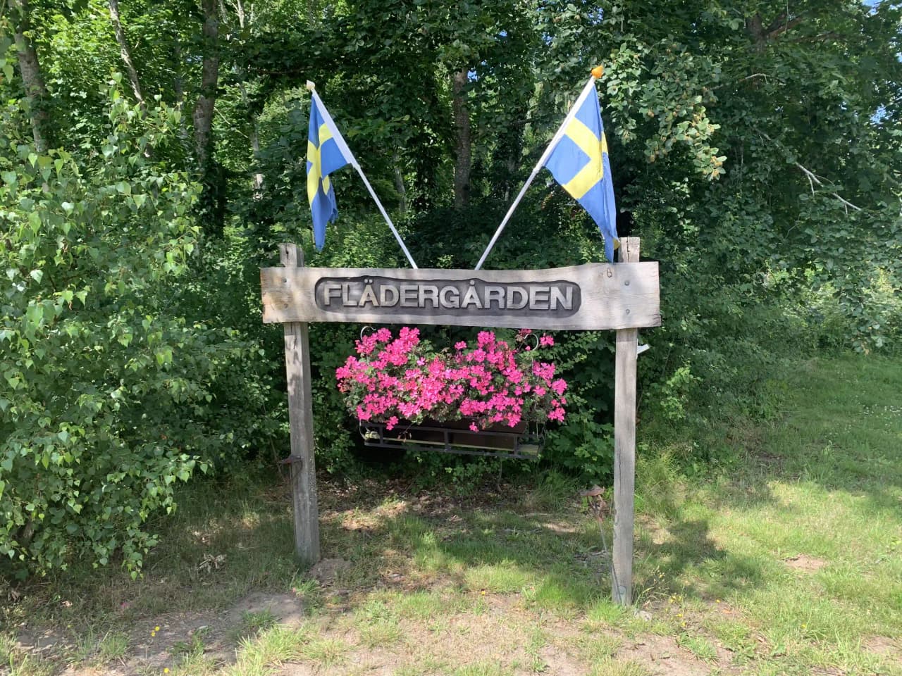 En lummig miljö med buskar och markväxter i vårblomning, som leder till en skyltmärkt stig på Vinslövs camping i en trädgårdsliknande park.