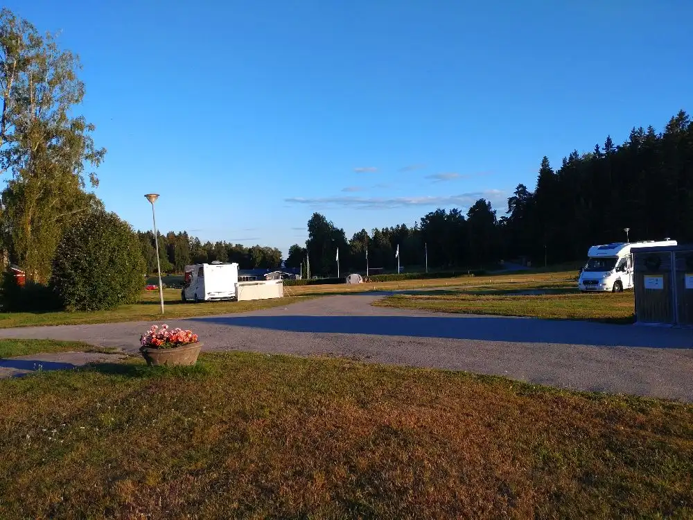 En husbil står parkerad på grusvägen vid Farstanäs camping & havsbad, omgiven av grönt gräs och träd i bakgrunden.