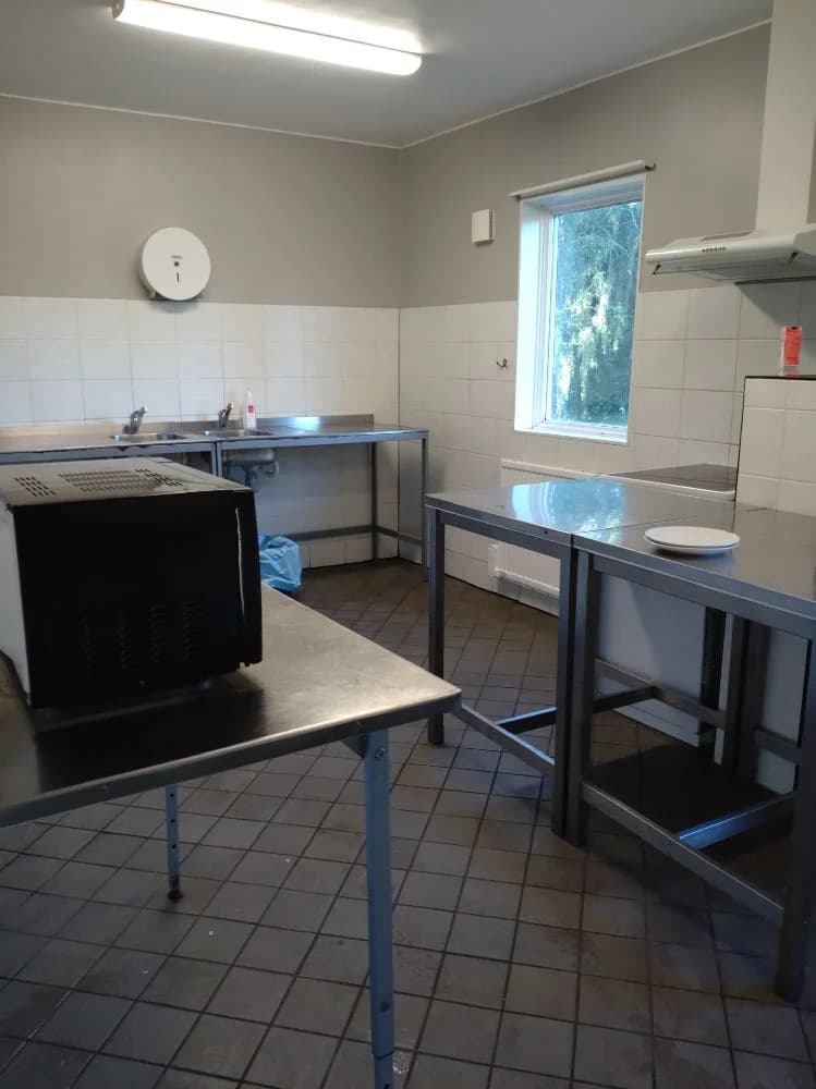 Ett modernt kök med silverfärgade vitvaror, inklusive en spis och kylskåp, samt ljusa bänkskivor och trägolv, vilket finns på Farstanäs Camping & Havsbad.