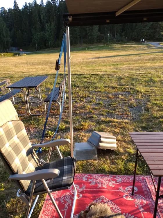 En campingplats med utemöbler som inkluderar fällbara stolar och ett bord. Möblerna står på en grön gräsmatta under solskydd, nära stranden på Farstanäs Camping & Havsbad.