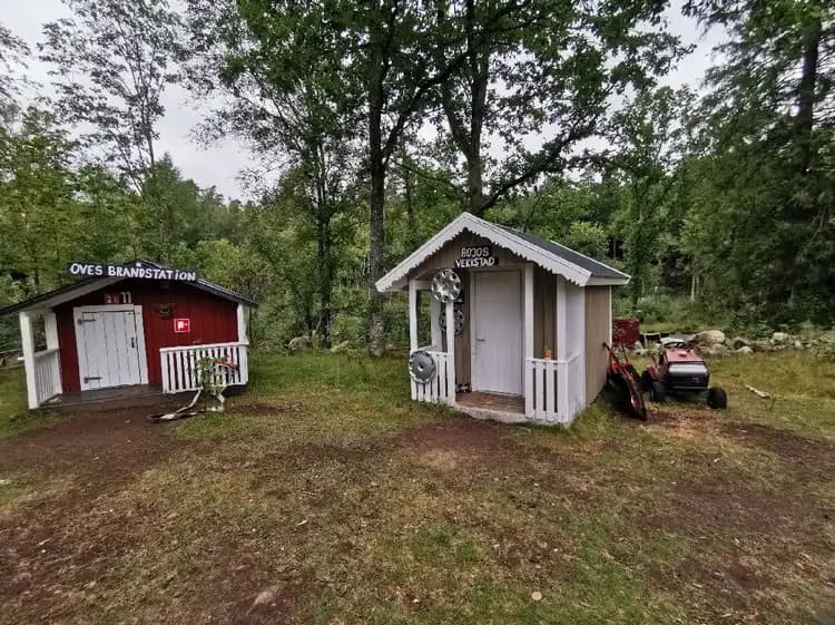 Ett träcottage på Gunnagård med ett tak och en dörr, omgivet av trädgårdsbyggnader och en bakgård.