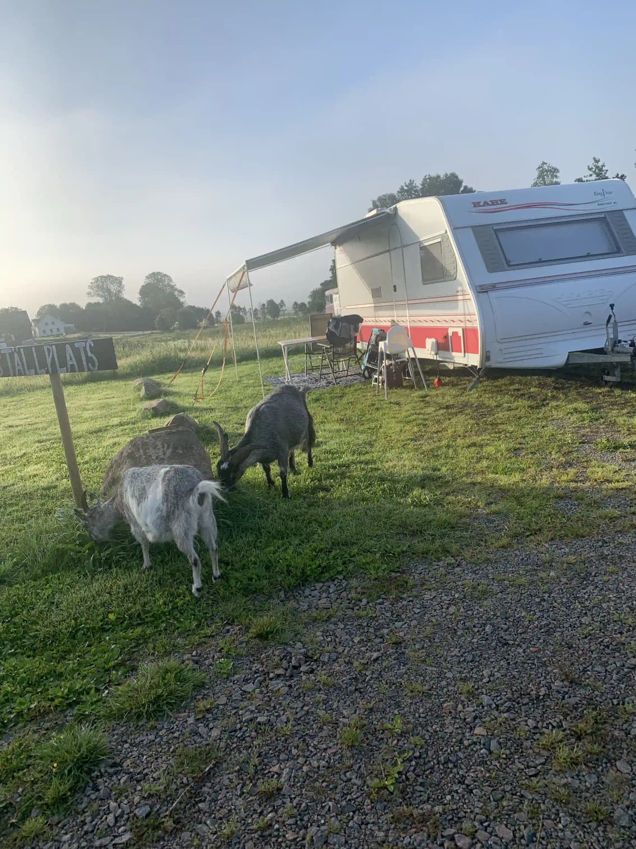 En husvagn står parkerad på en gräsmatta vid Gunnagård, omgiven av öppna fält och landsbygdsmiljö.
