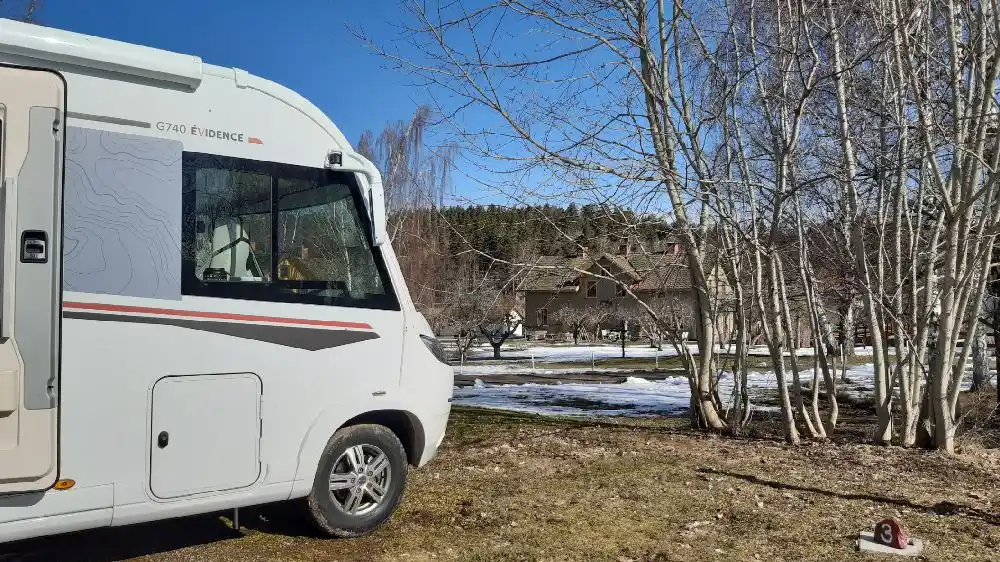 En mobil hem- och husbilspark vid ett glasbruk, med flera husvagnar och husbilar parkerade på platsen, omgivna av grönska och skog.