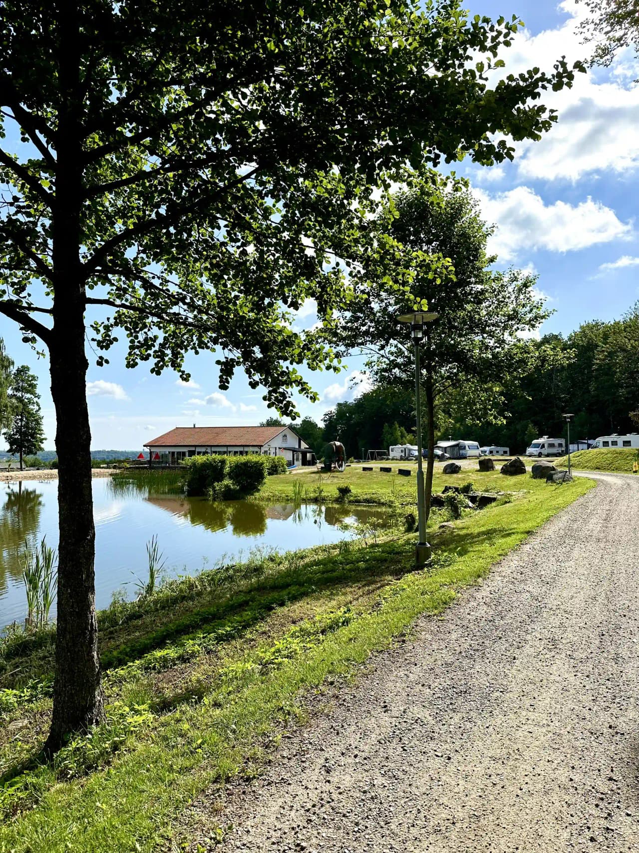 Bilden visar en naturskön vy över en stillsam sjö omgiven av grönska vid Tostarps camping, läger- och kursgård. Sjön speglar himlen och träden runtomkring, och skapar en harmonisk och avkopplande atmosfär i det lantliga området.