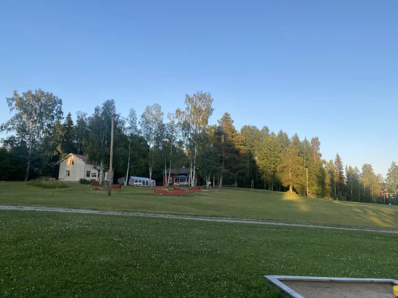 En grönskande campingplats vid Valasjön omgiven av träd och gräs, med öppna ytor för rekreation.