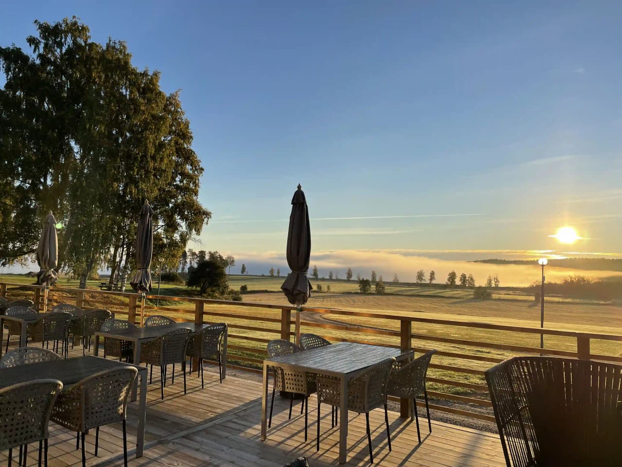 En utomhusmiljö vid Älvstalodges med trämöbler på en uteplats. Bord och stolar i hårt trä under ett solskydd, omgivna av dämpad kvällsbelysning.