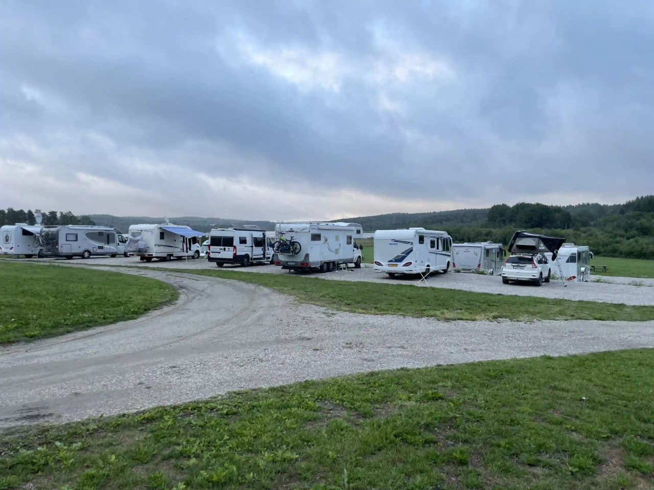 En husbil och en lastbil parkerade på en grusplan under en blå himmel med vita moln.