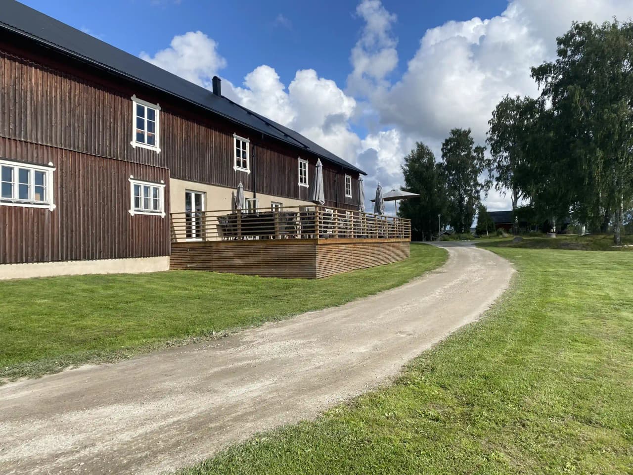 Bild av älvstalodges: En mysig stuga med träpaneler omgiven av en grönskande trädgård, belägen på en lantlig gårdsmiljö.