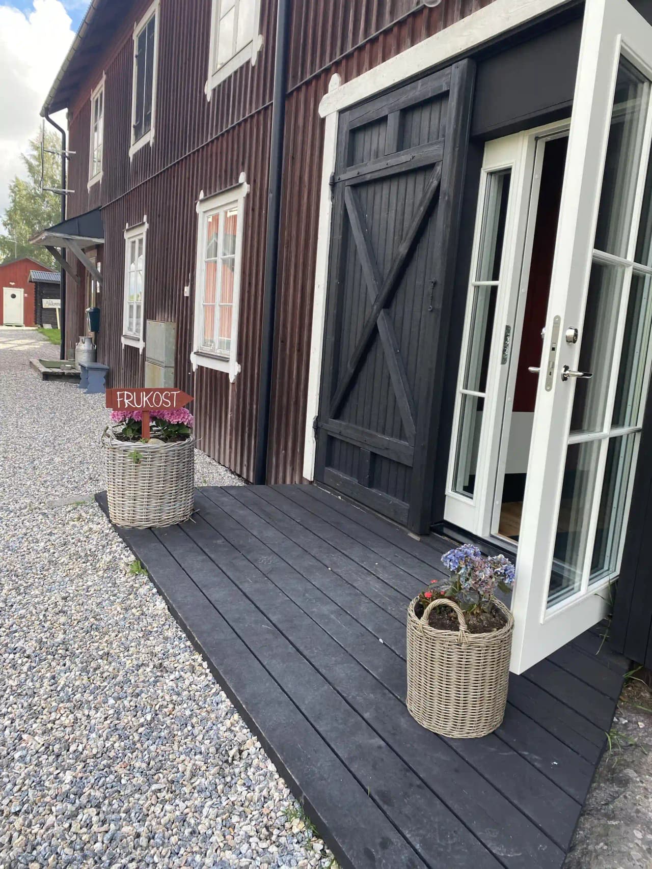 Bild av en träfasad med dörr, blomkruka och veranda, omgiven av en välskött trädgård vid Älvstalodges.