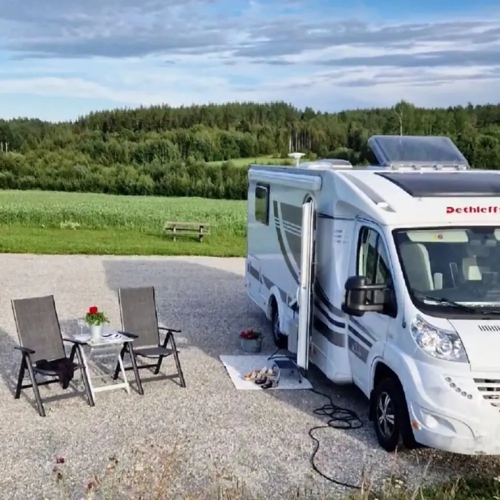 Bild på en husvagn och husbil uppställda på en campingplats vid Älvstalodges. Husvagnen och husbilen står parkerade på grus och omgivningen präglas av skog och natur.