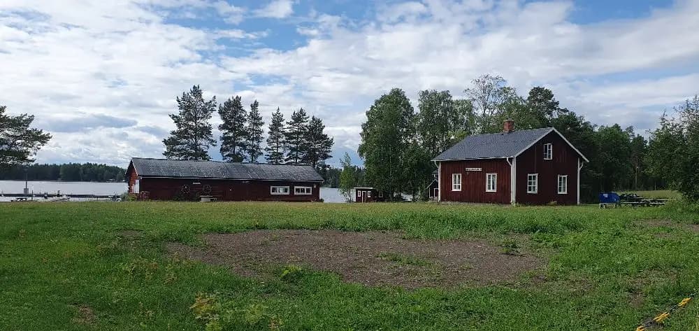 En lantlig stuga ligger inbäddad i ett grönt gräslandskap under en molnig himmel vid Kungsgårdsviken.