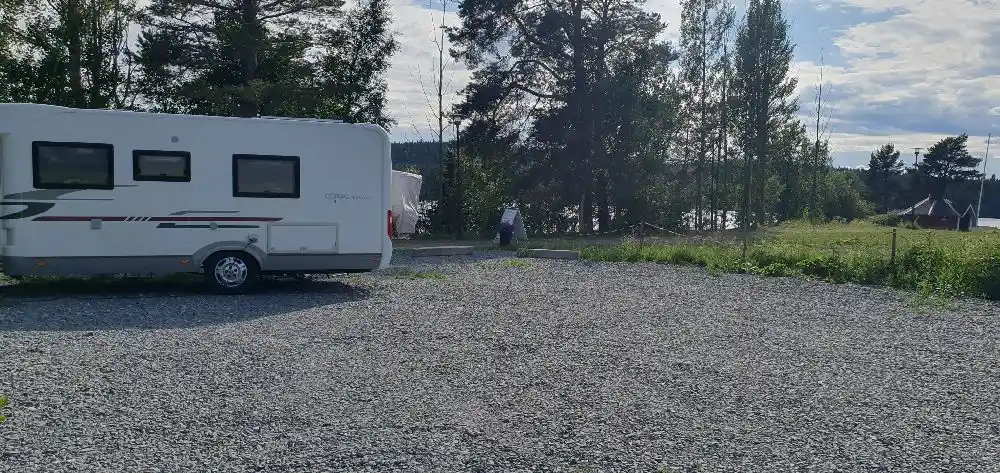 En husvagn och en husbil är parkerade på en grusväg nära en gräsmatta vid Kungsgårdsviken, vilket ger en känsla av en campingmiljö.