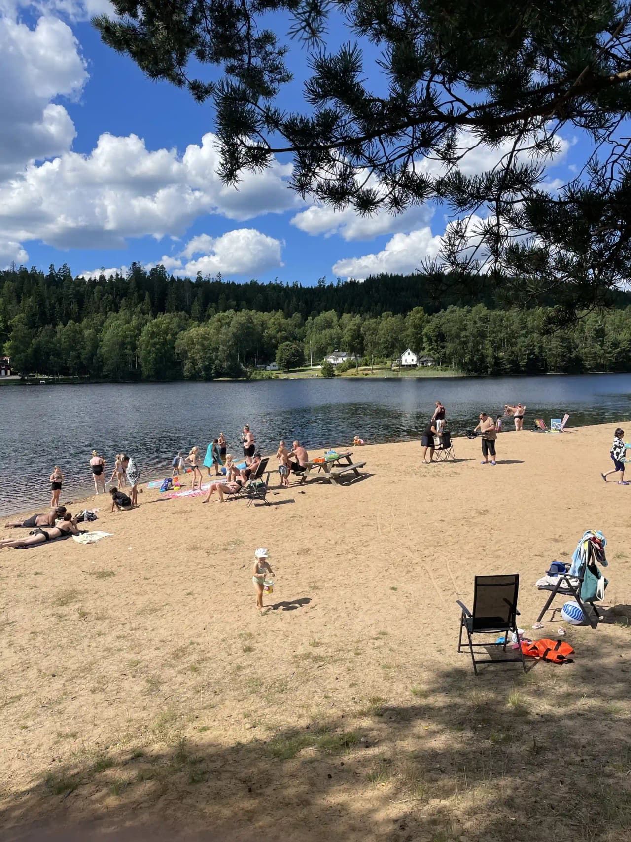 En sjö med en sandstrand där människor njuter av fritidsaktiviteter vid vattnet på Överlida Camping.