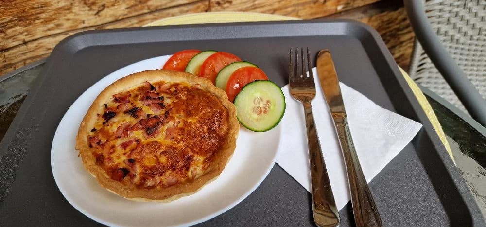 En nygräddad pizza med rikliga ingredienser serverad på en vit tallrik. Tallriken står på ett träbord tillsammans med bestick och servetter.