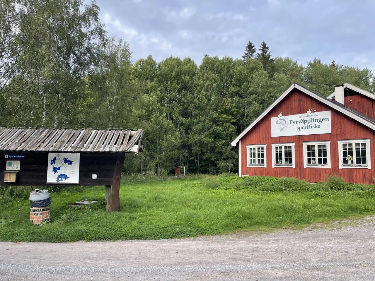 En grönskande gårdsplan med en timmerstuga, en ladugård och ett förråd i naturlig miljö. Perfekt för ett besök i lantlig idyll.