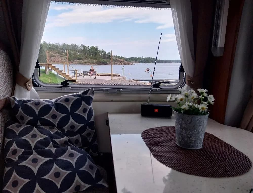 En husbil och en husvagn parkerade vid Eriksviks hamn, med vatten och båtar i bakgrunden.