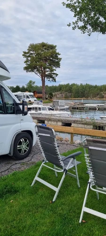 En uteservering vid Eriksviks hamn med flera hopfällbara stolar och bord. En parasoll står uppställd och i bakgrunden syns en parkeringsplats.