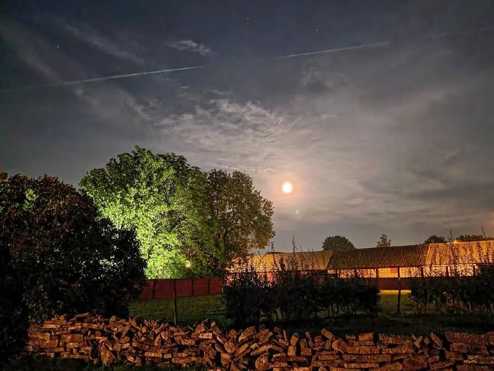 En stämningsfull kvällsbild över Kalvhagen i Södvik med klar himmel och en lysande fullmåne i bakgrunden, omgiven av naturens stillhet i skymningsljus.