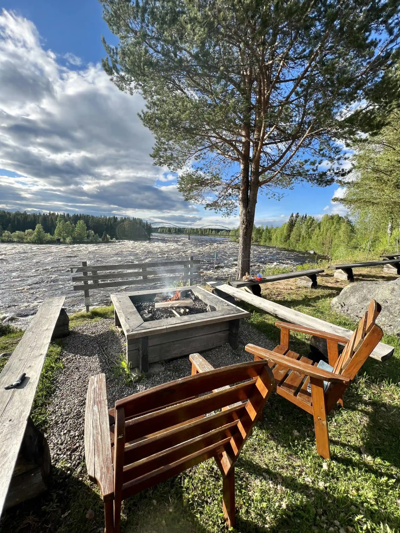 En picknickplats vid Kamlunge camping med träbord och bänkar. Platsen ligger vid stranden, omgiven av skog och natur.