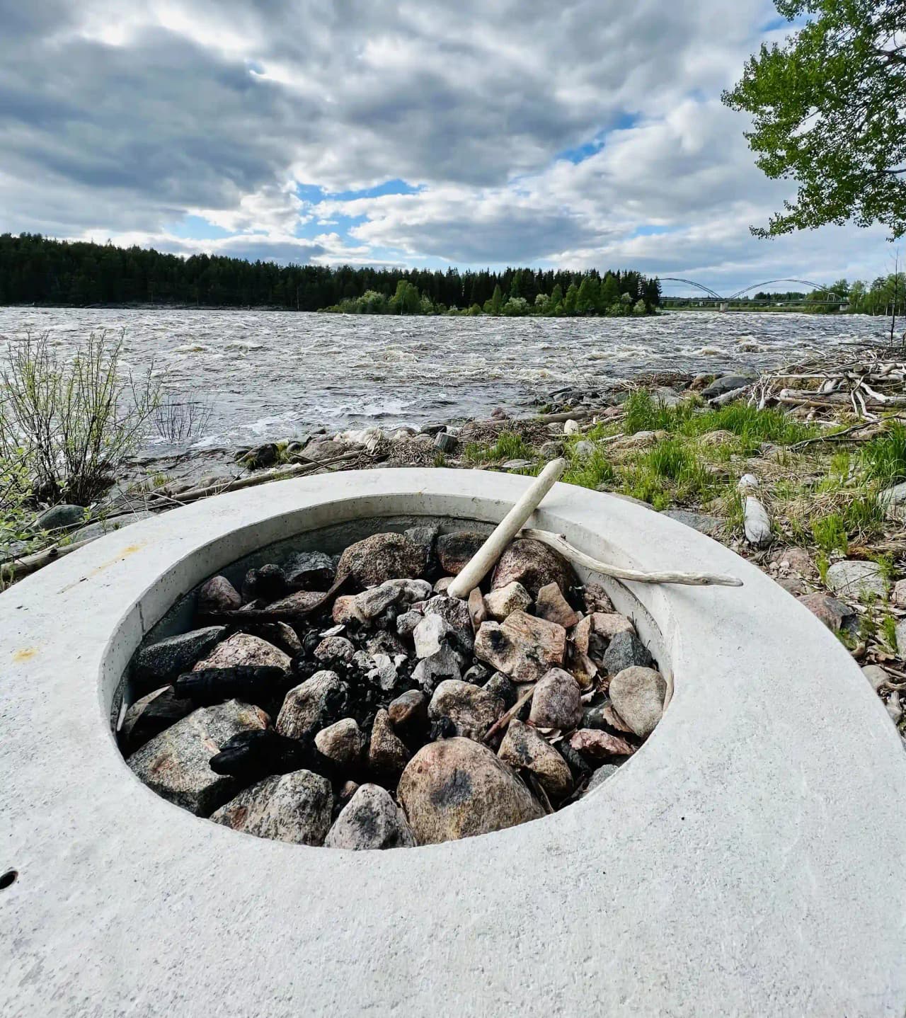 En småstensstrand vid Kamlunge Camping, med naturliga material och frodig grönska i bakgrunden.