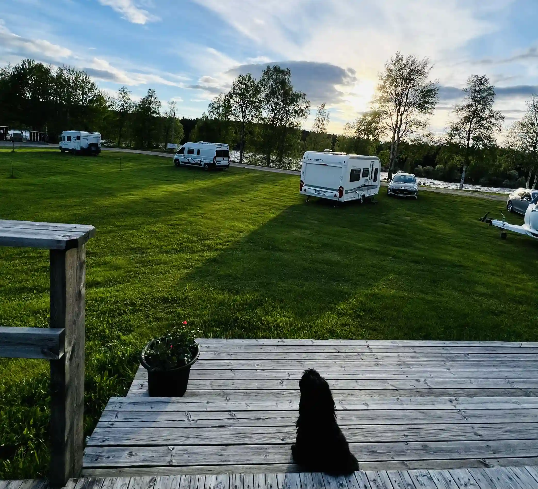 En öppen campingplats med gräs och ett husvagnsområde under en molnig himmel.
