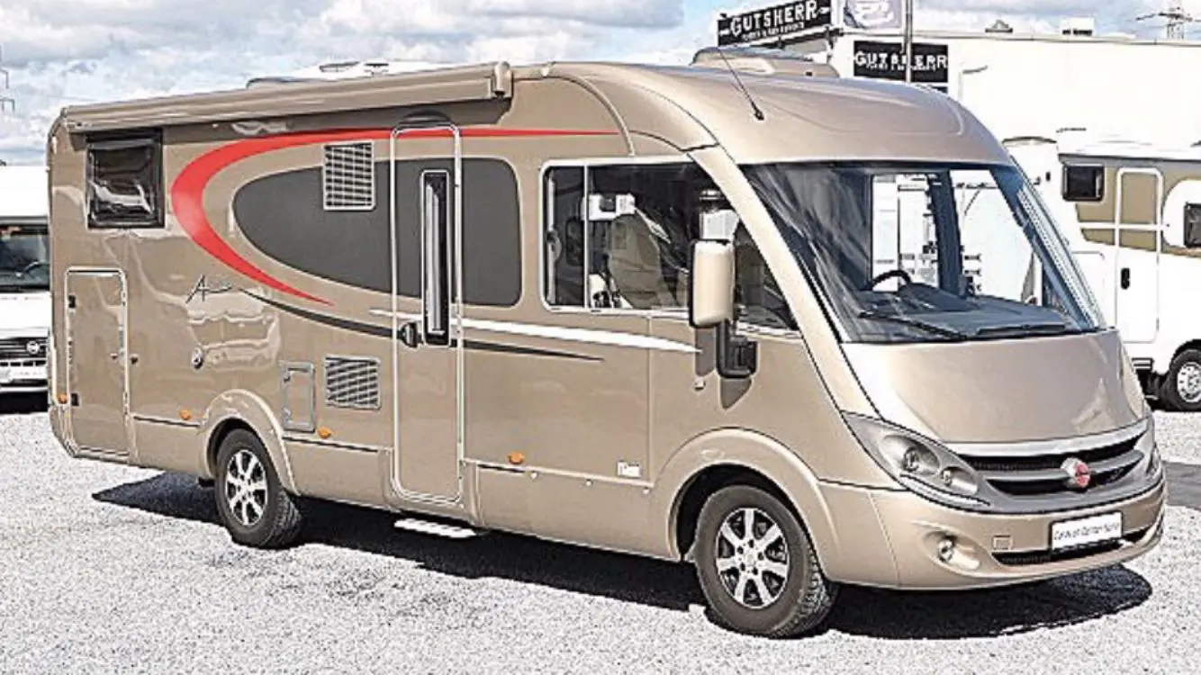 En klassisk bil står parkerad vid Hätte camping, nära en husbil. Bilens detaljer som kofångare, fälgar och backspegel är tydligt synliga, omgiven av natursköna omgivningar som campingplatsen erbjuder.