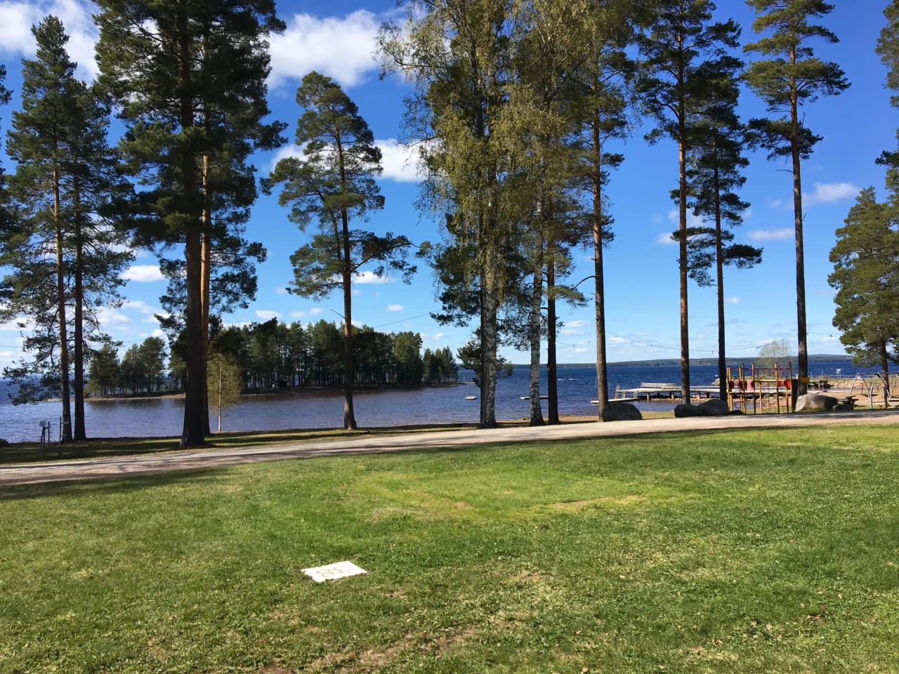 En stilla insjö kantad av träd och skuggor, med en grönskande campingområde vid stranden i den natursköna Tällberg.