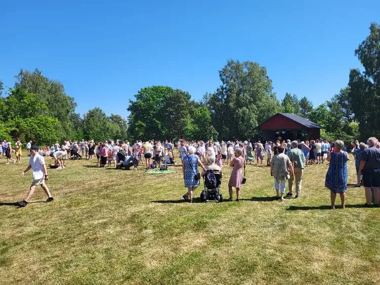 En folksamling njuter av våren vid Kaffetorpets camping, omgiven av träd och grönska. Platsen används för fritidsaktiviteter och sociala evenemang.