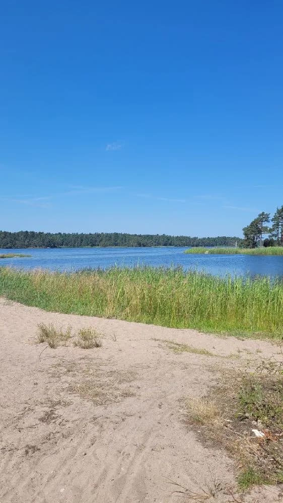 Bild av Kaffetorpets camping visar en blå himmel som möter en bred vattenyta. Landskapet är naturligt med en vattenväg som korsar scenen och omges av frodiga, gröna stränder. Horisontlinjen är tydlig och speglas lätt i det lugna vattnet.