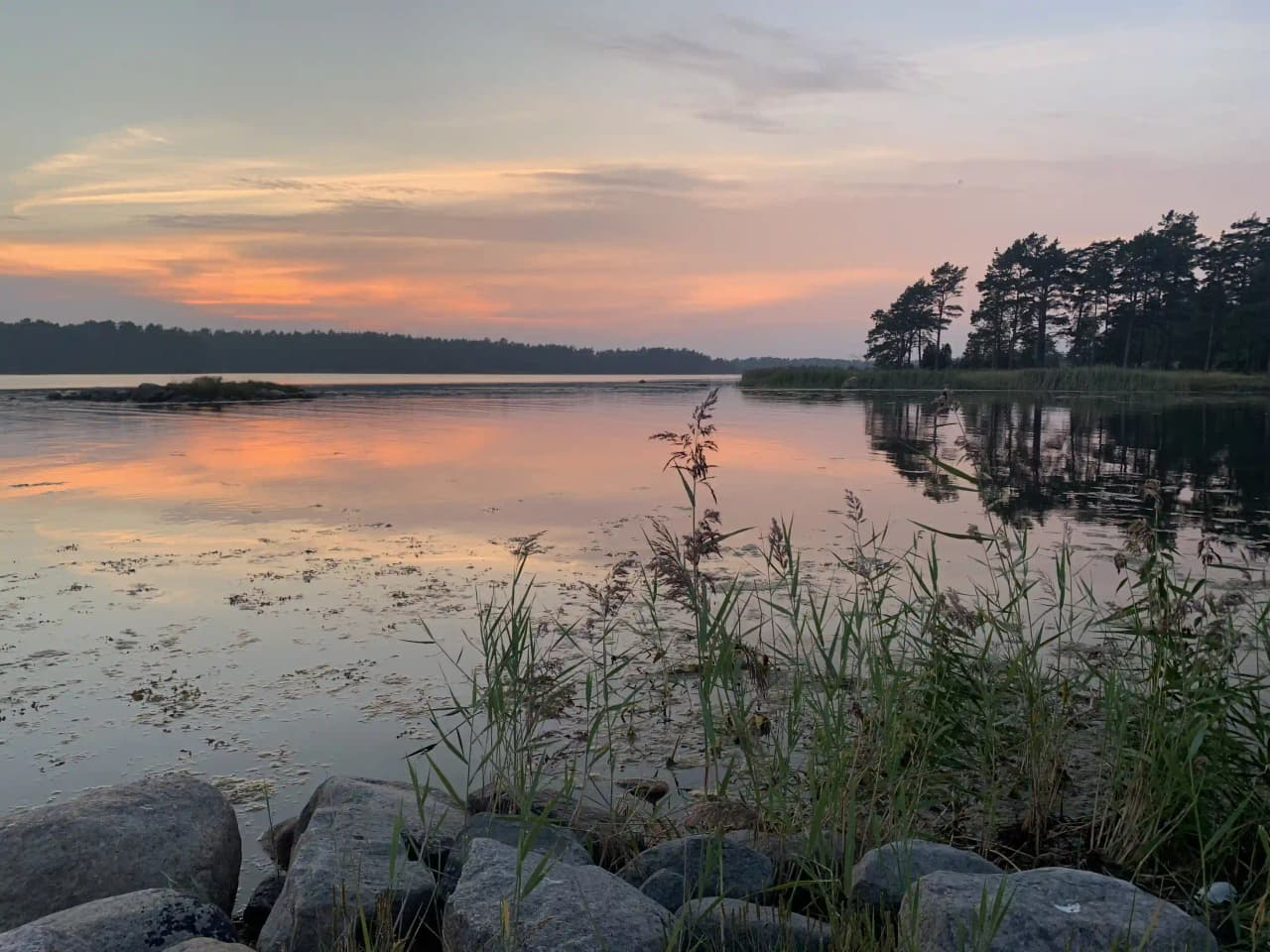 En naturskön vy vid Kaffetorpets camping med en himmel i skymningsljus, speglat i vattnet som omges av frodig natur.