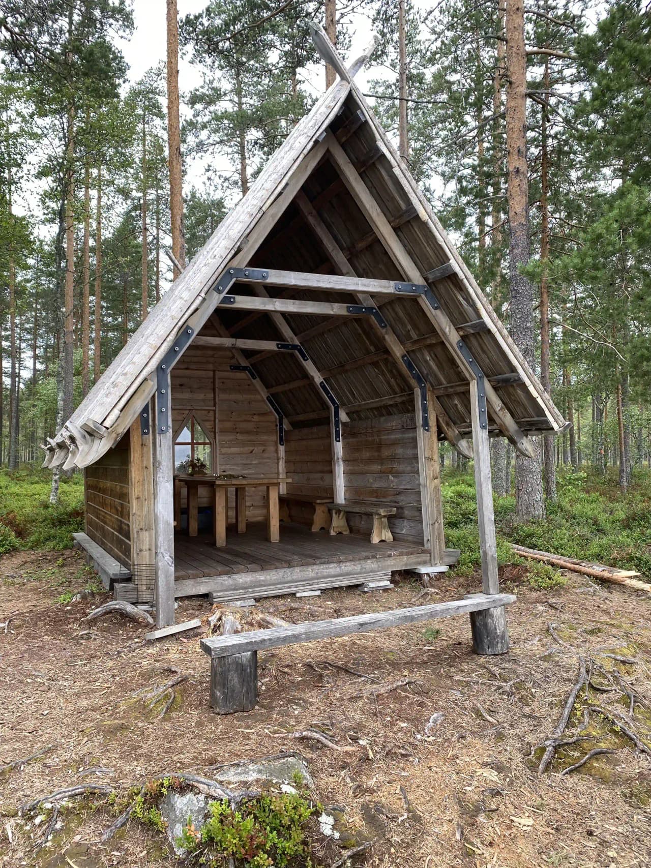 En trästuga omgivet av grönska, med ett snedtak och väggar av träplankor, vid Åsengården.