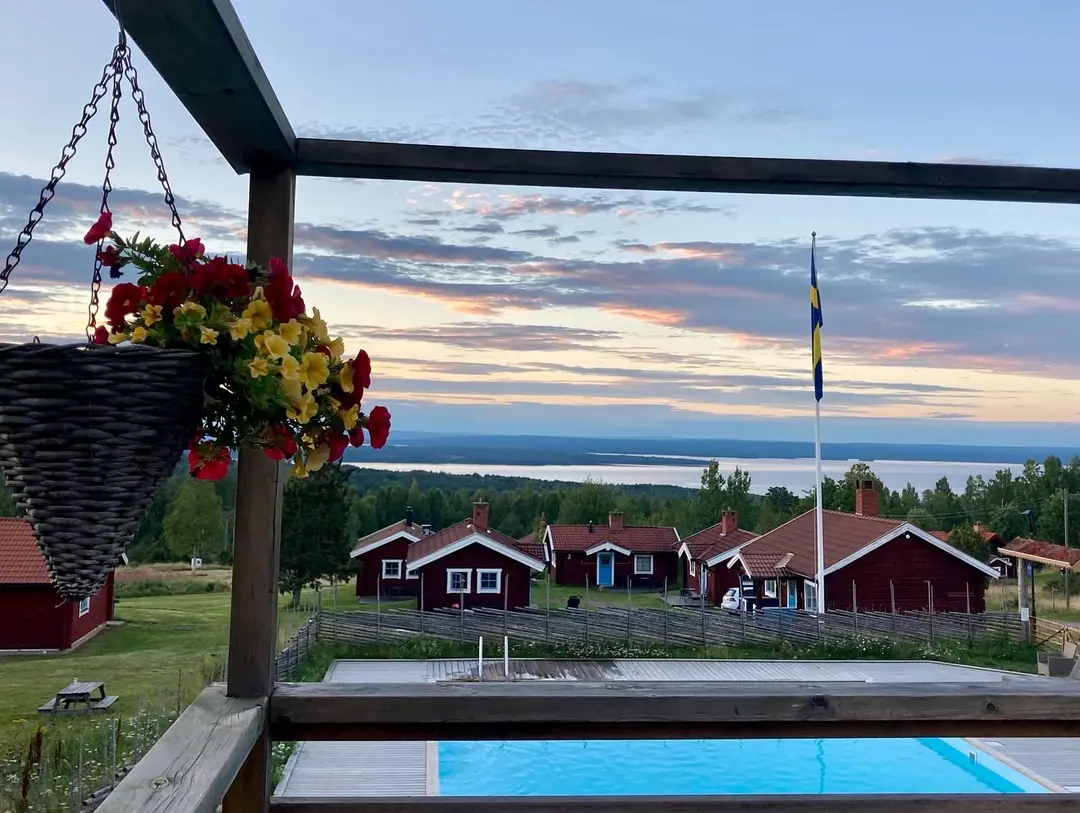 Utomhusmöbler på en gårdsveranda med skuggande tak. Stolar och ett bord står på en stenlagd uteplats, omgivna av grönska. Perfekt för avkoppling och njutning av den lantliga miljön vid Åsengården.