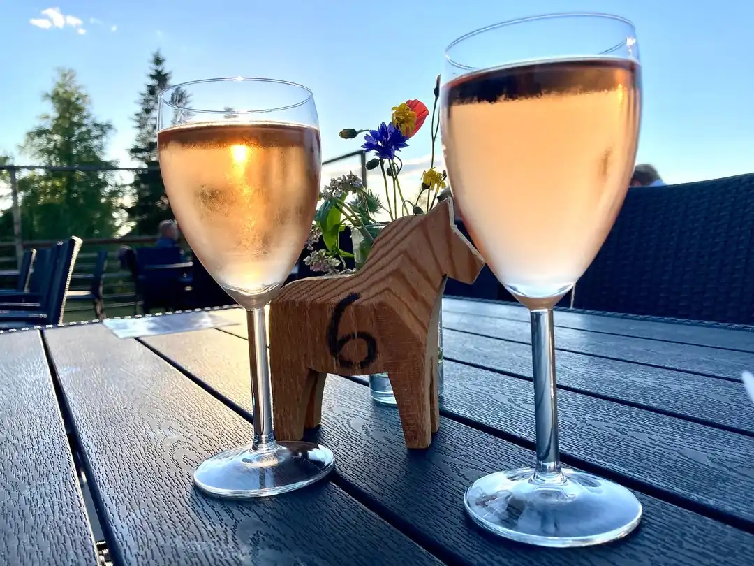 En elegant uppsättning av glas och drinkar på ett dukat bord, med fokus på vinglas och andra dryckesglas. I bakgrunden syns en varm och inbjudande miljö, som kan vara en del av inredningen på Åsengården.
