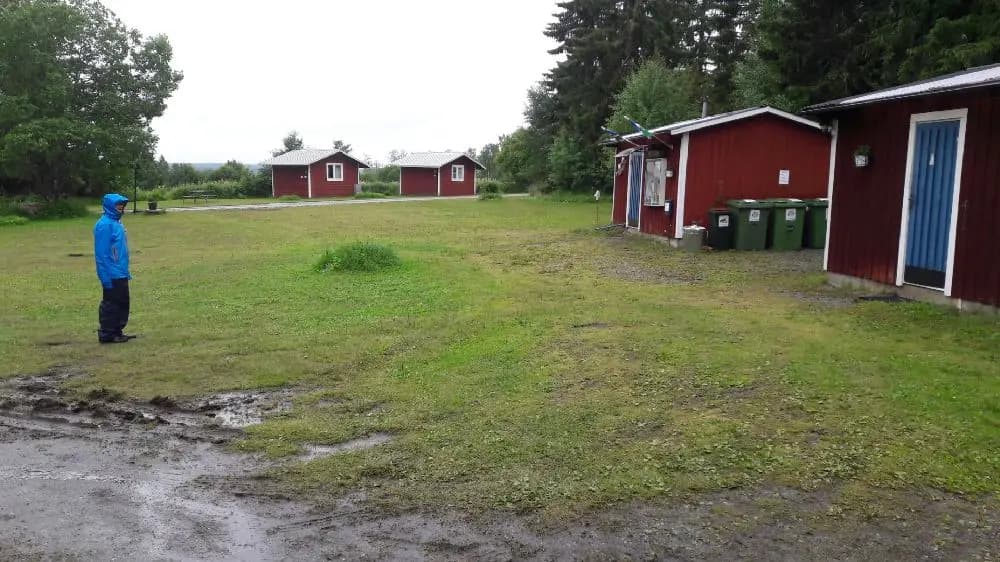 En grön campingplats med gräsmattor och pittoreska stugor, omgiven av öppna landskap, vid Ångsta Camping.