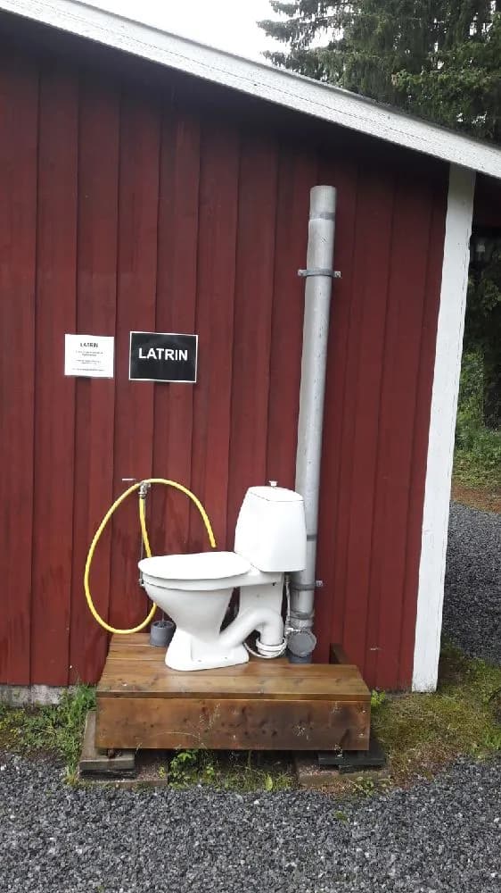 Alt-text: Bilden visar ett rent och prydligt badrum med en toalettstol och rörmokeri, del av faciliteterna på Ångsta camping.