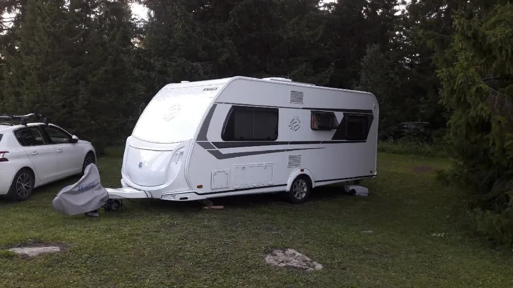 En husvagn och en bil står parkerade vid Ångsta camping, omgivna av grönska.