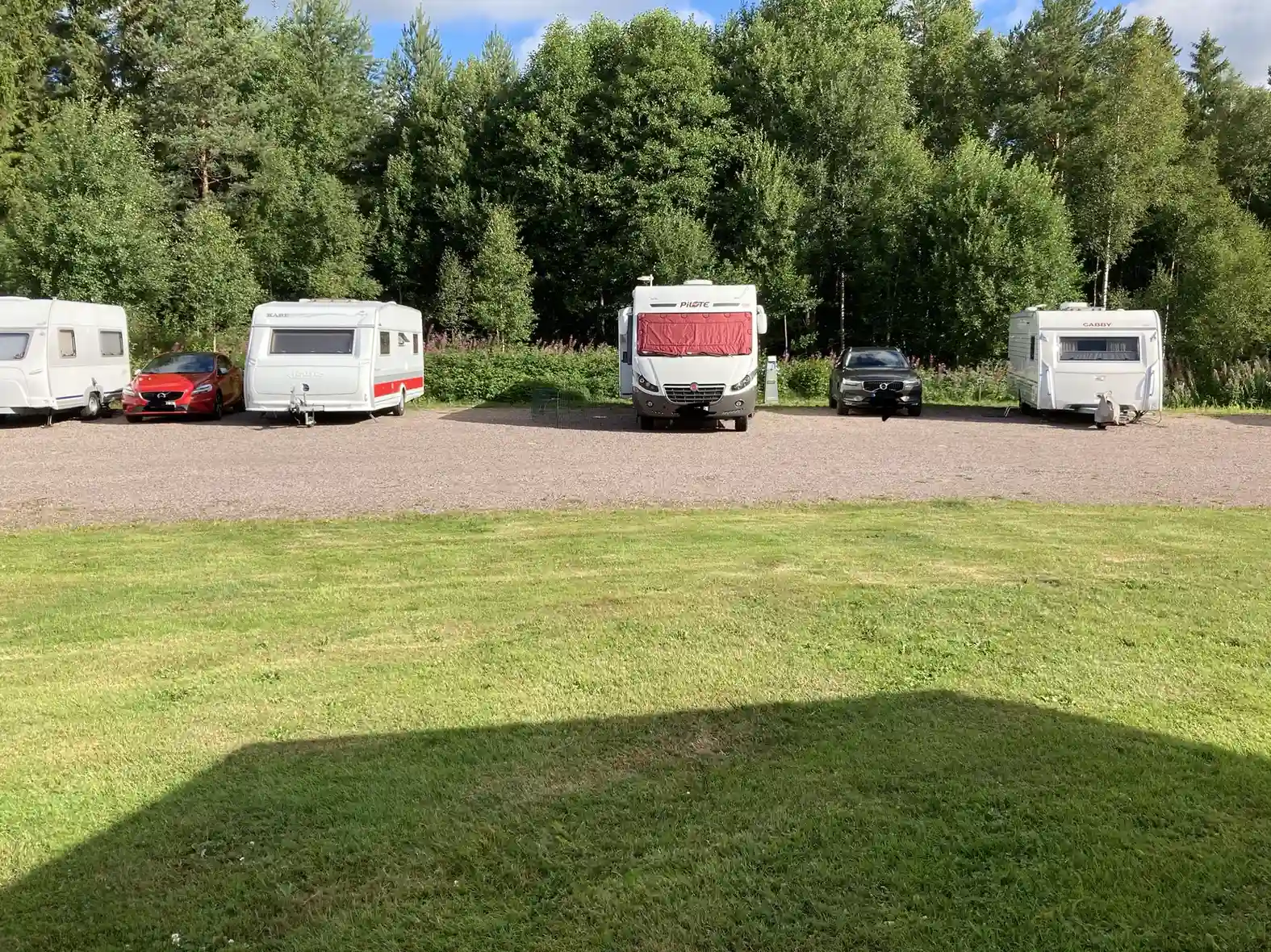 En husvagn står parkerad i en naturskön miljö på Lovsjöbadens camping, omgiven av grönska och med en rymlig uppställningsyta.