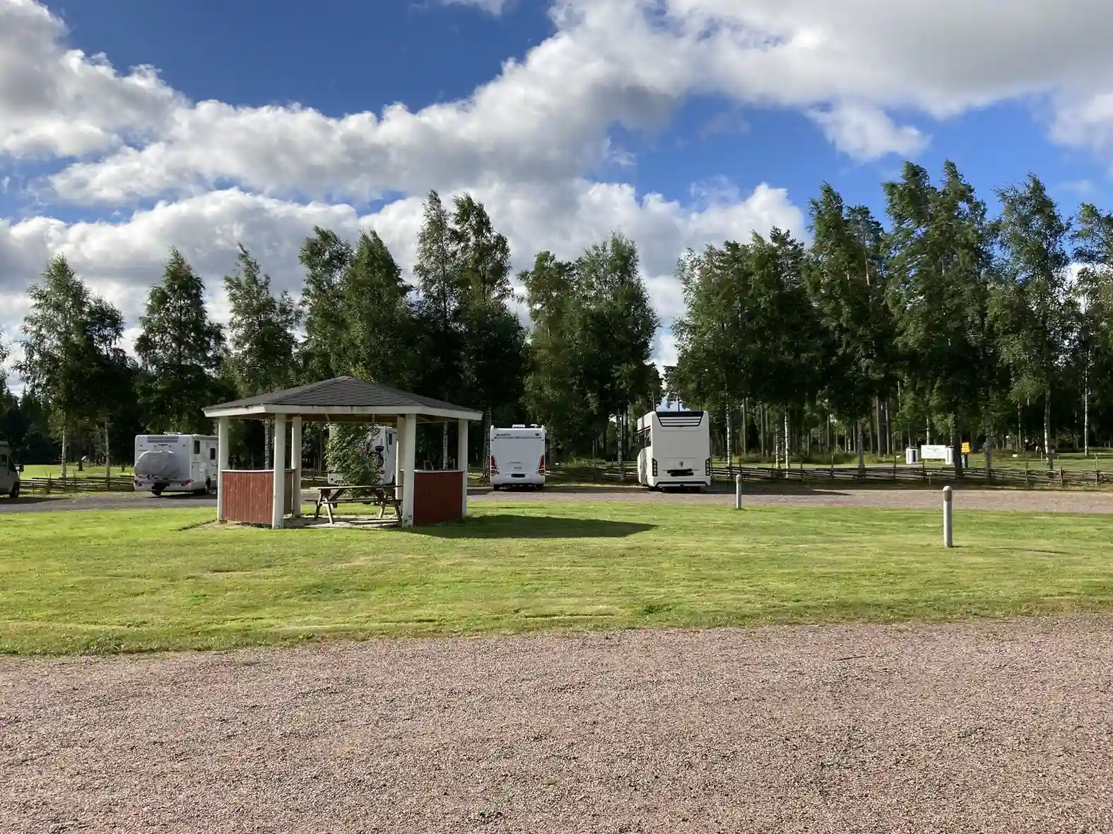 En husvagn och en husbil parkerade på gräsmattan vid Lovsjöbadens camping, omgivna av öppna ytor och skuggiga träd.