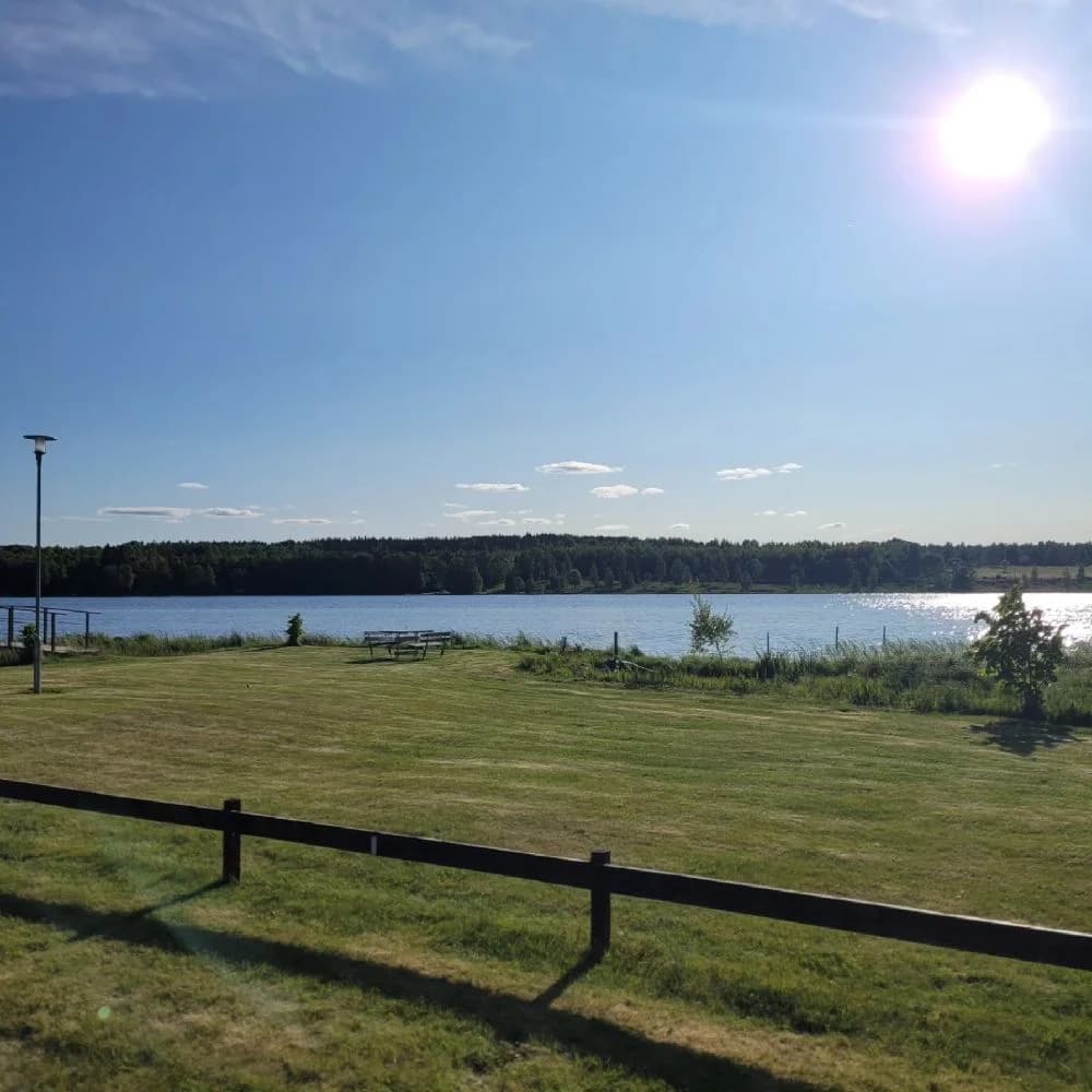 En vidsträckt campingplats i Målsånna med gräsytor och en klar himmel. Vyn sträcker sig mot horisonten med moln som svävar över fält och ängar. En rofylld morgon med en anlagd gräsmatta som inramar platsen.