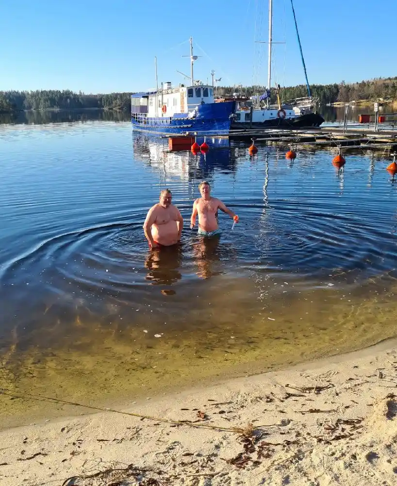 En vy över Upperuds Gästhamn där flera båtar ligger förtöjda vid bryggor längs en stilla vattenväg, omgivna av grönskande natur.