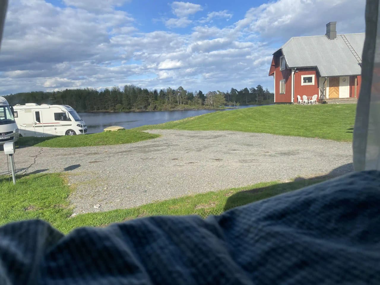 Bild av Upperuds Gästhamn: En naturskön plats med en grön gräsmatta vid vattnet, omgiven av sjölandskap och molnig himmel. Perfekt för camping och friluftsaktiviteter.