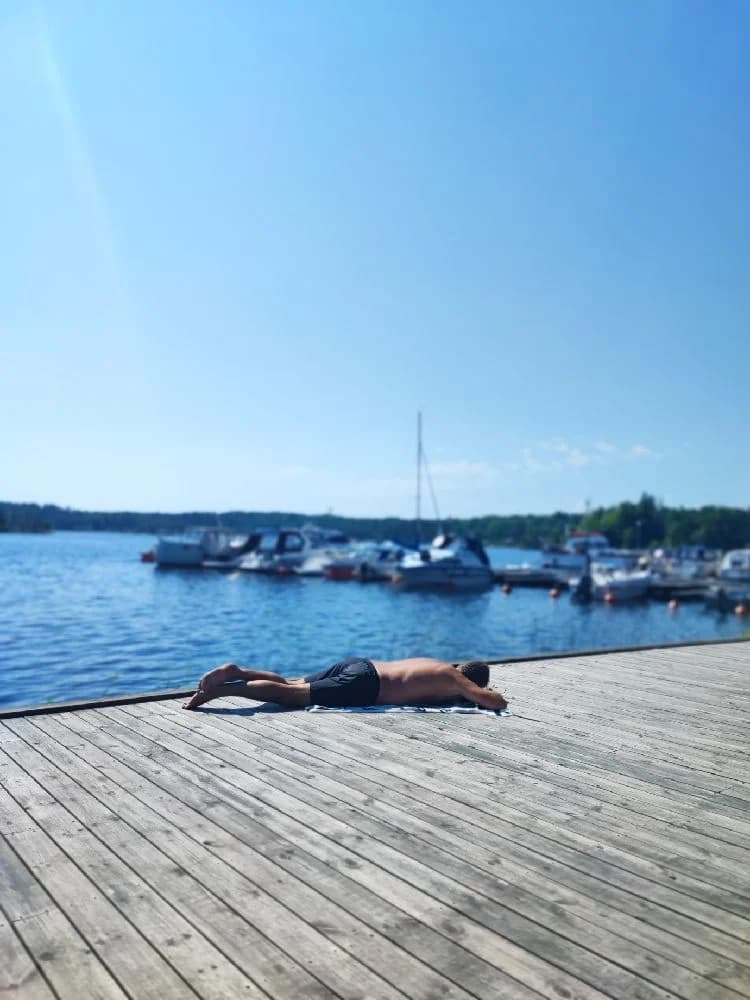 Bild av Upperuds Gästhamn en solig sommardag, med en brygga vid en sjö där människor njuter av fritid och semesteraktiviteter.