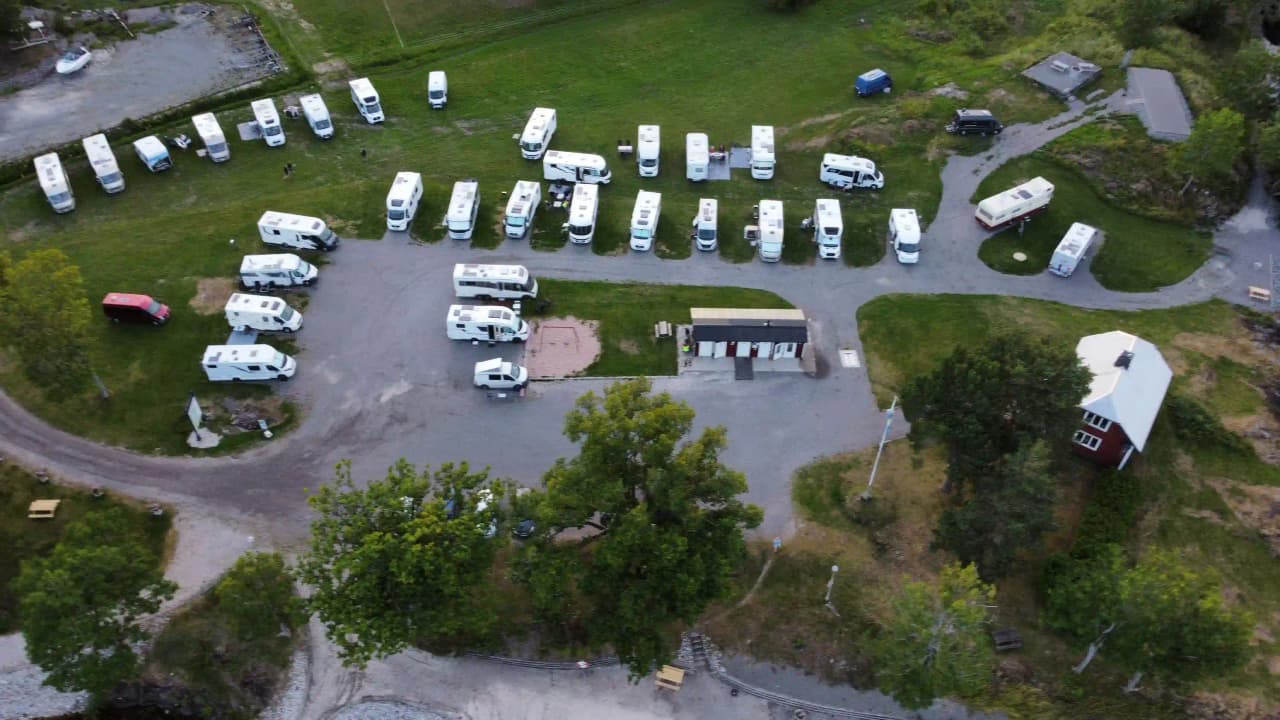Luftbild av Upperuds Gästhamn med parkerade husbilar och bilar på en grusbelagd parkering vid hamnområdet, omgiven av grönska och vatten.