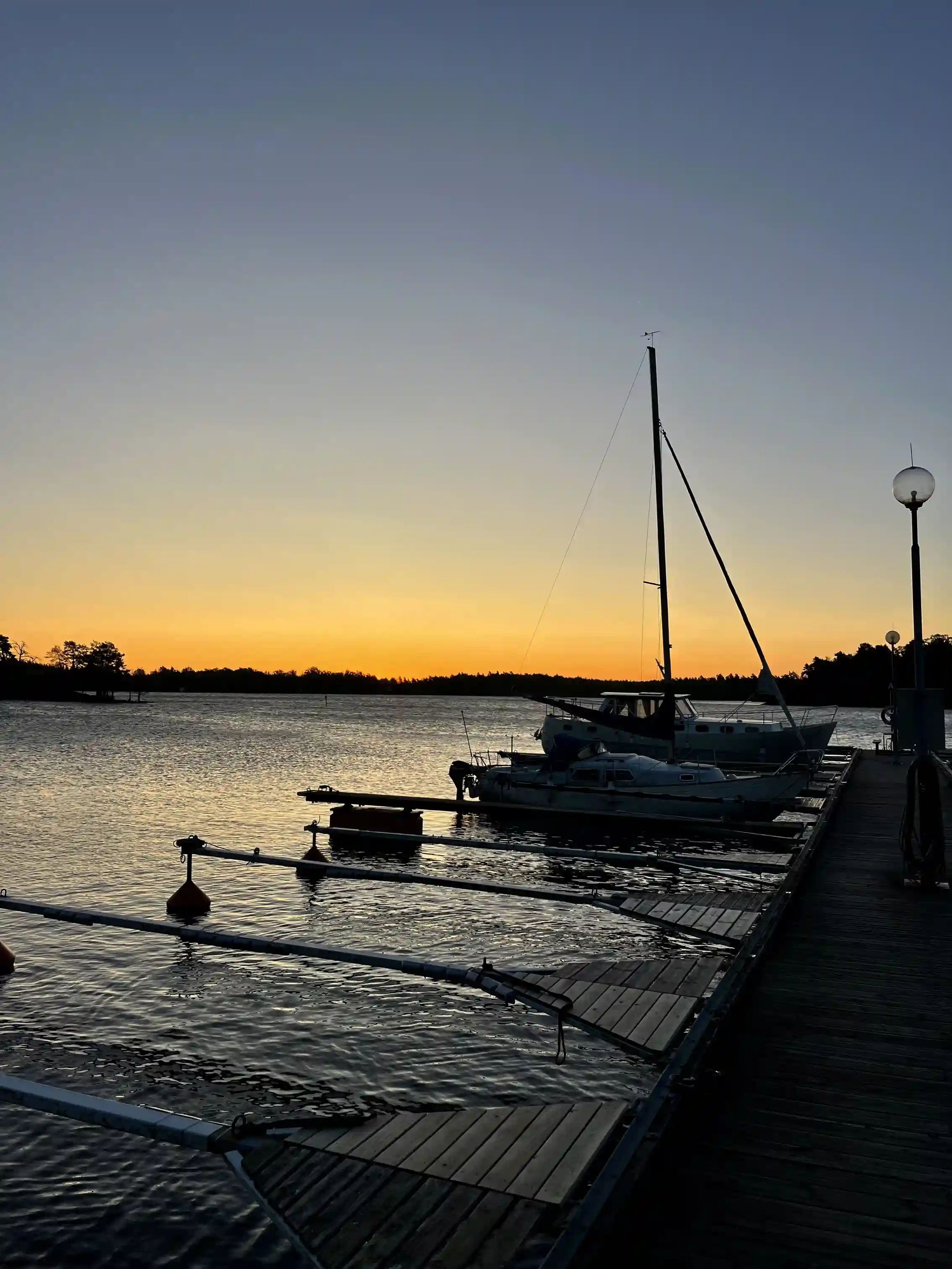 En stilla hamn vid solnedgång med båtar förtöjda i vattnet, omgivna av ett gyllene sken vid horisonten.