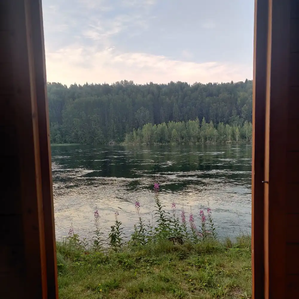 En pittoresk sjö omgiven av skog i kvällsljus, med speglingar av träden på vattenytan.