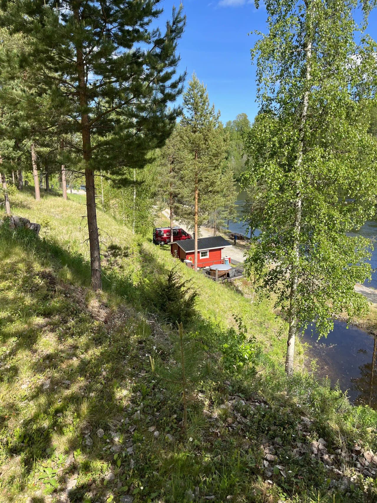 En naturskön bild av en grönskande landsbygd med gräs och träd, där en liten stuga ligger omgiven av skog och öppna fält. Passar som besöksmål på Zorbcenter.