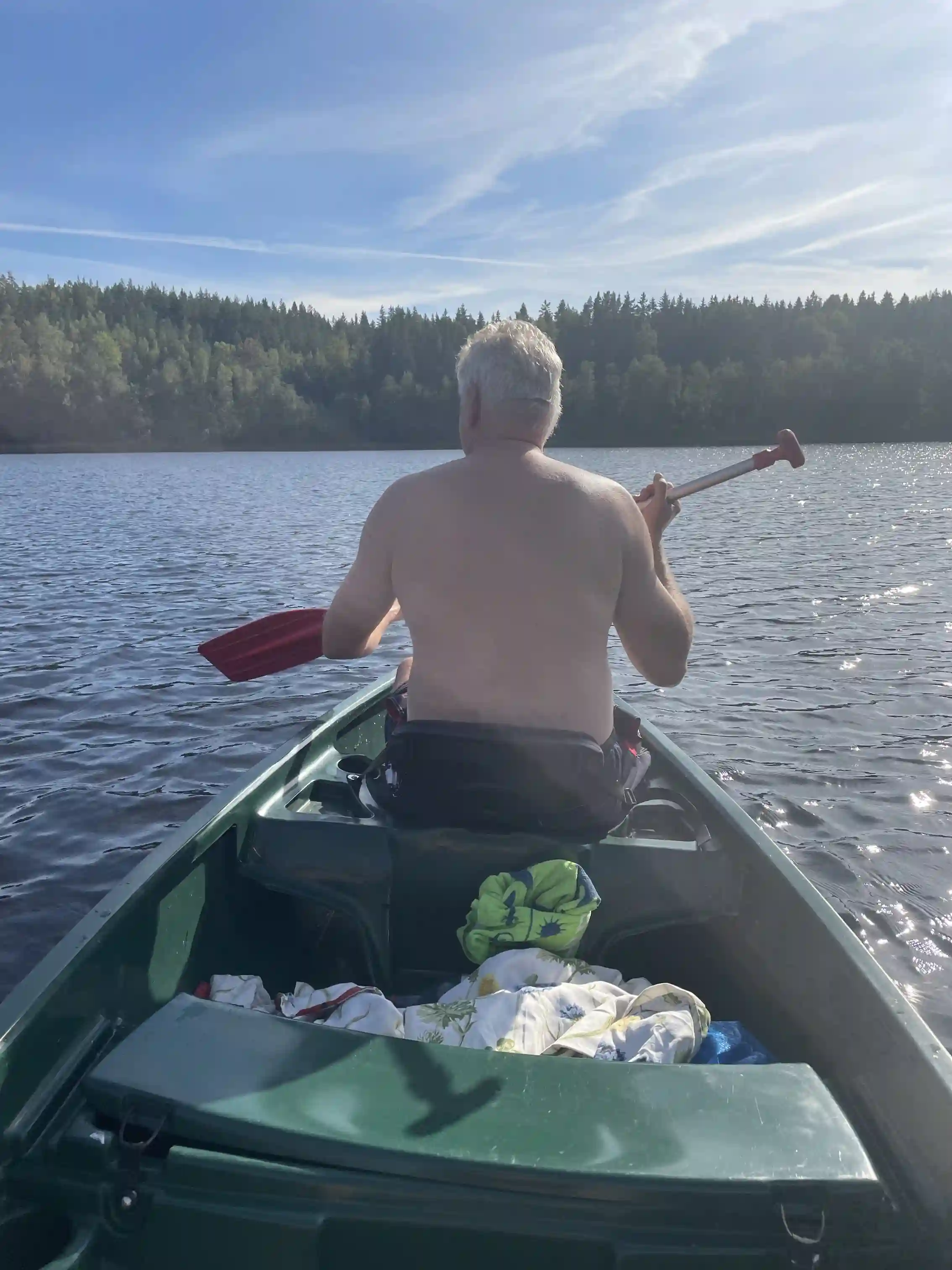 En kanot med paddlar flyter på en lugn sjö vid Amundebo Södergård, omgiven av grönska och speglar den natursköna miljön.