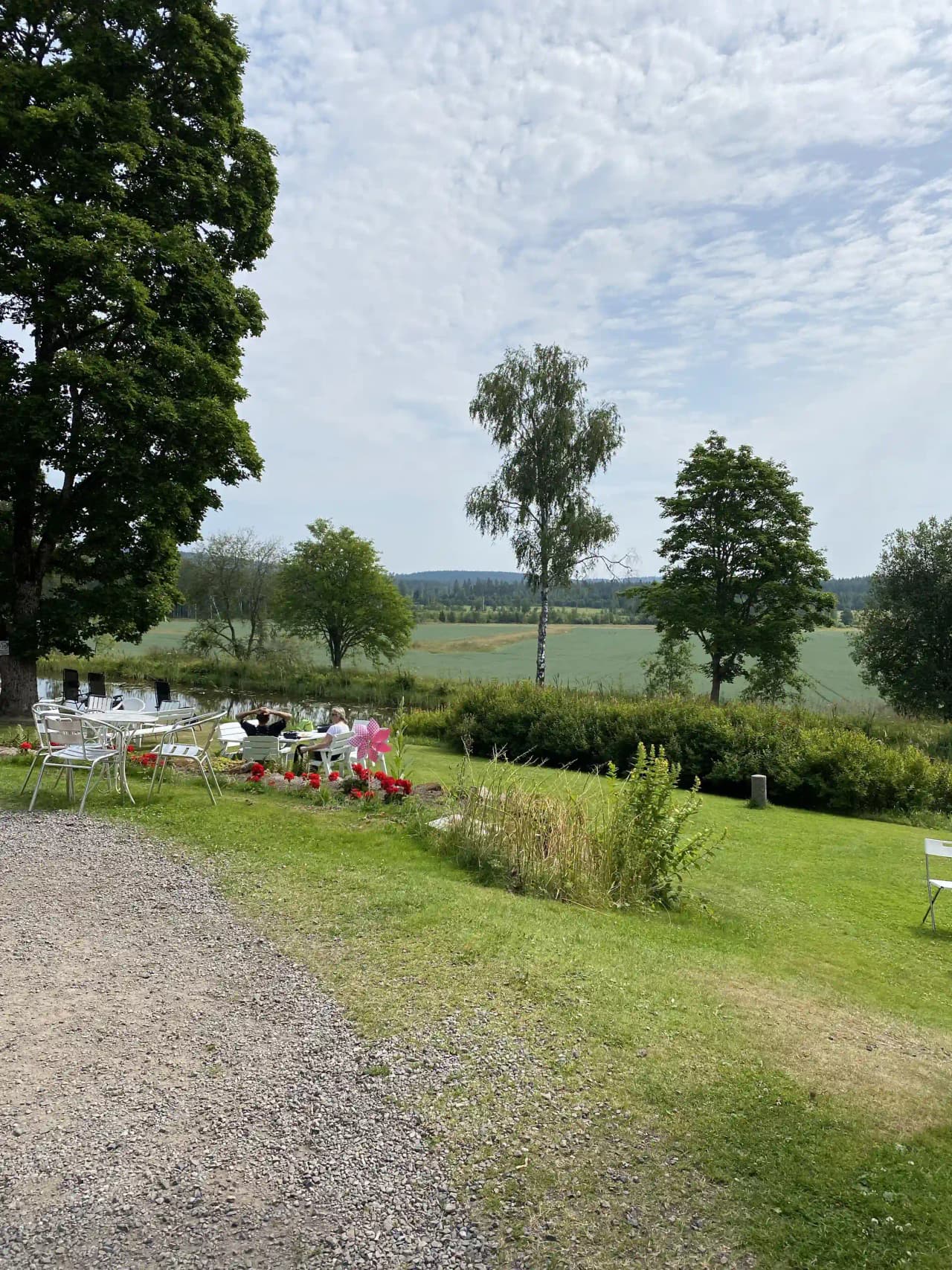 En naturskön campingplats med frodig växtlighet och buskar. Gräsmattor och utomhusmöbler är utspridda i området, vilket skapar en inbjudande miljö för avkoppling och umgänge under våren.