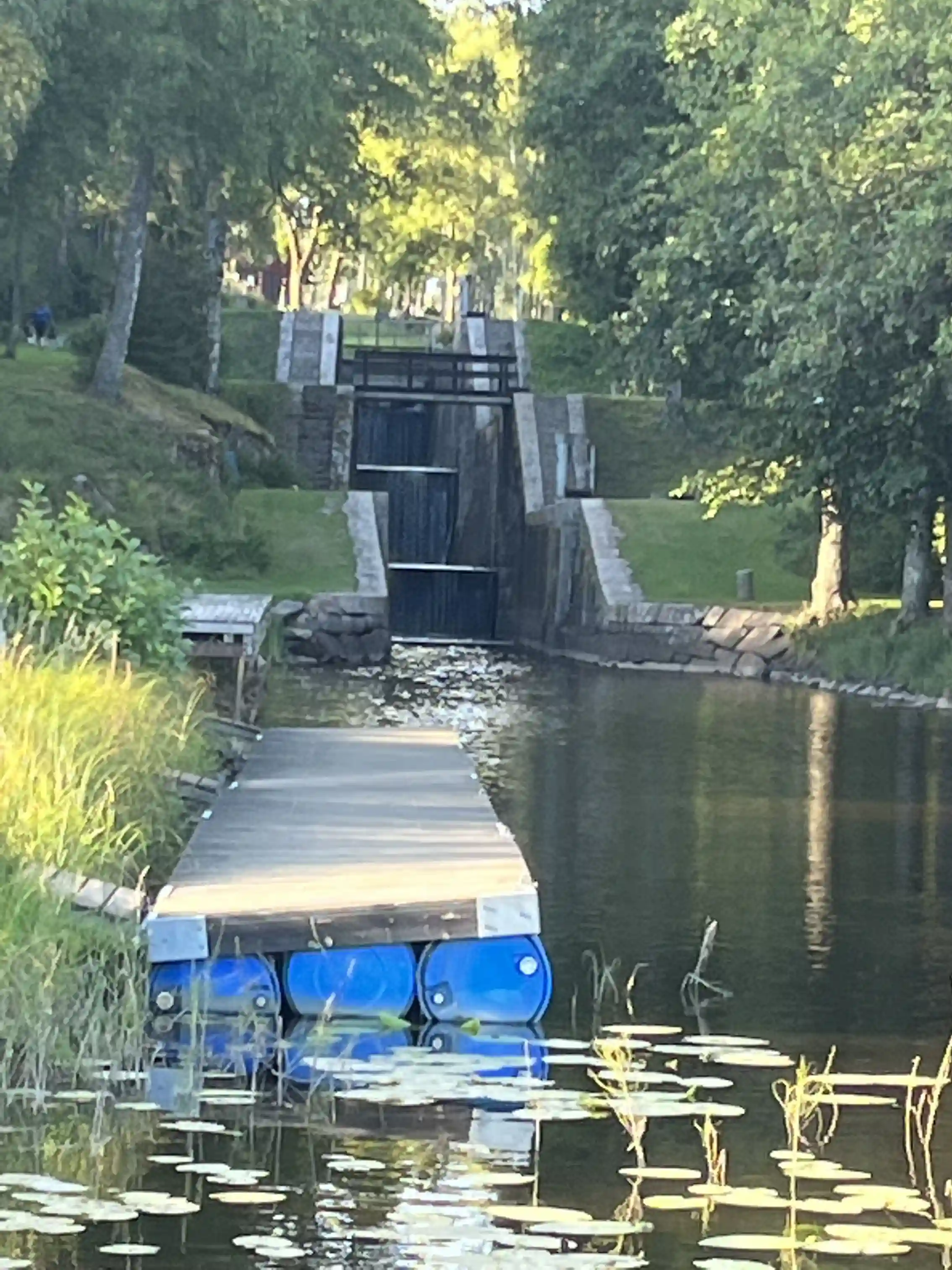 En lugn vattenyta vid Badsta camping med spegelblank reflektion, omgiven av grönskande kanter och en stillsam kanal.